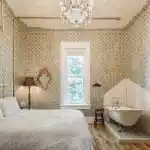 The Victorian Room inside Urban Cowboy Nashville, lit with a warm light of the chandelier. A king sized bed is placed in the middle, just across from a tiled area holding a claw foot bathtub.