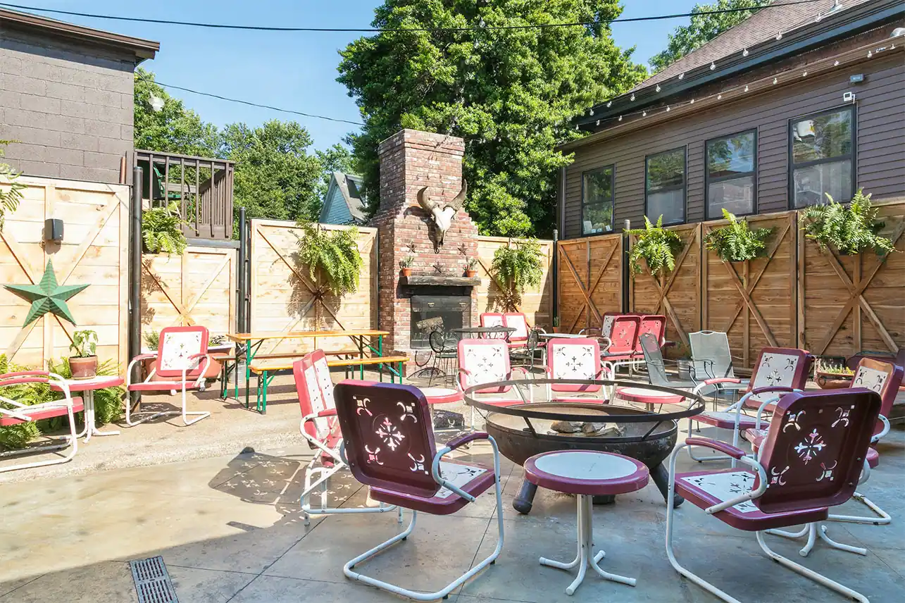 Outdoor Patio of Urban Cowboy's Public House. Bench seats and table/chairs are scattered. A stone fireplace is set up towards the back.