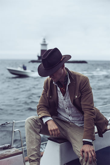 Man with a cowboy hat looking downward as a boat takes him on the water.