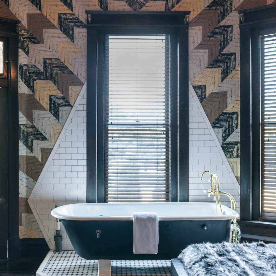 View of a bathtub inside The Midnight Rider accommodation inside Urban Cowboy Nashville. The tub is near the king sized bed, placed atop a tiled area shaped like a diamond along the wall. This octagonal room is set with three tall windows.