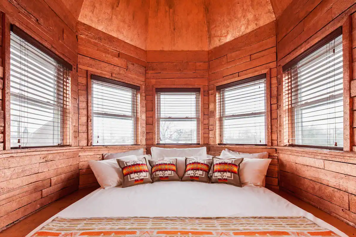 Bedroom space of The Tower room inside Urban Cowboy Nashville. A king sized bed takes up most of the space, with a set of small pillows lining the head. The ceiling is domed and windows line along each wall.
