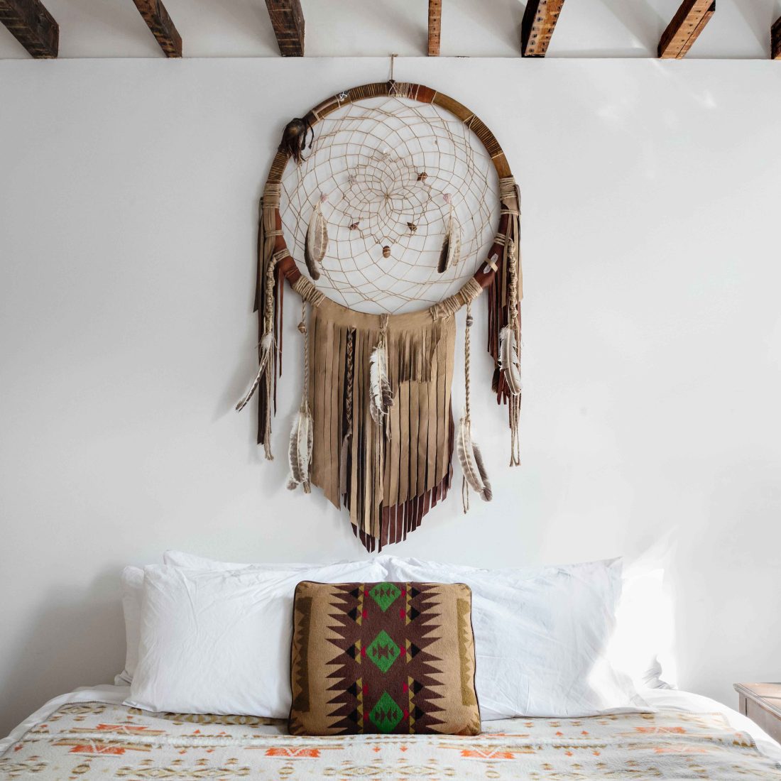 King sized bed inside the Dream Catcher room of Urban Cowboy Brooklyn. A large fringed dreamcatcher hangs above the bed.