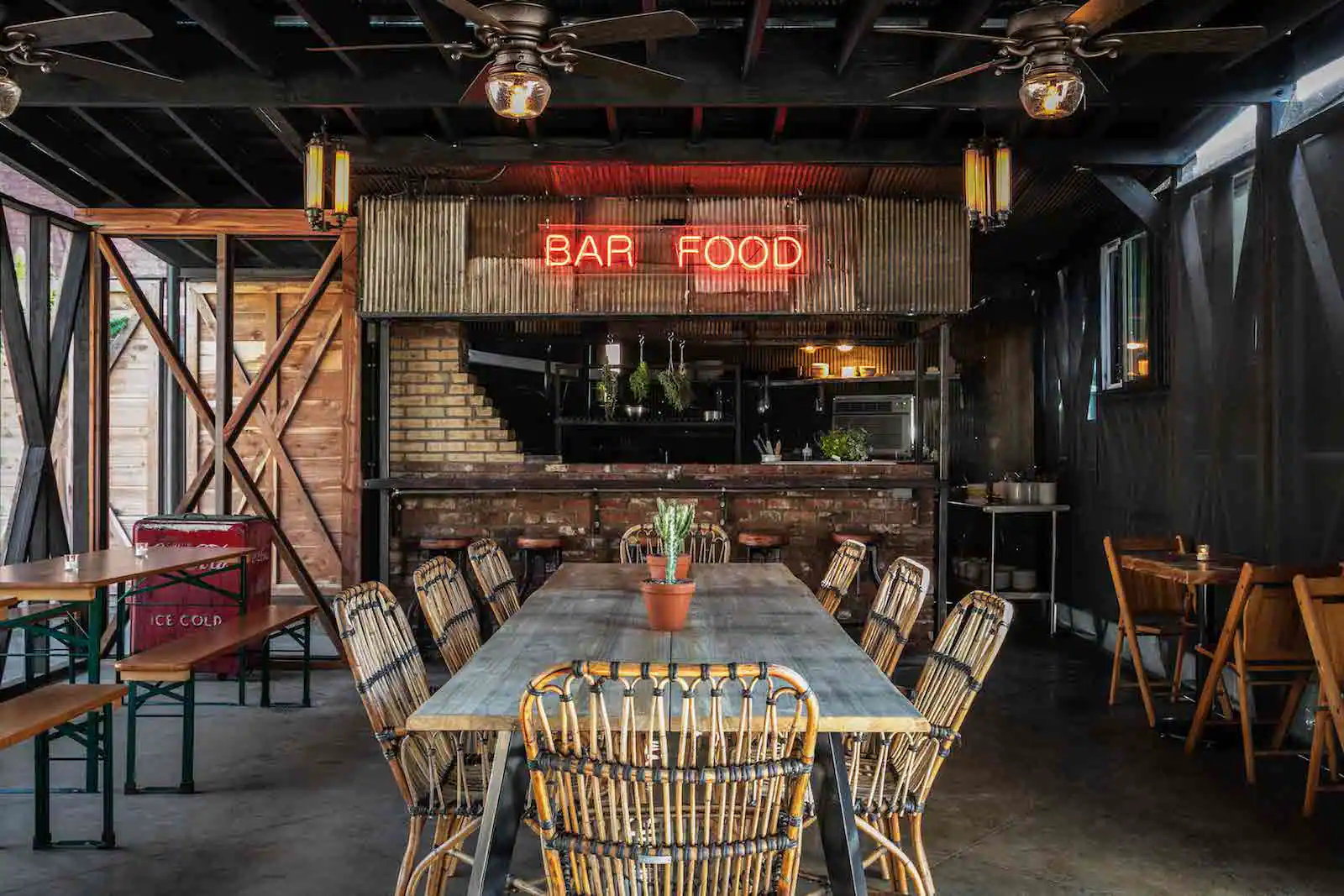 View of the main dining area of Urban Cowboy's Public House Kitchen and Bar. Woven chairs make up the area in the center, with wooden benches and tables in the areas beside.