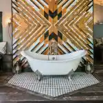 The clawfoot bathtub of The Cabin, inside Urban Cowboy. Geometric shapes are worked into gold reflective shapes behind.